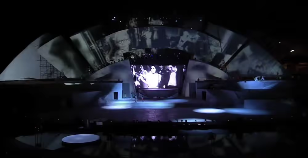 Black and white projections on the upper structure and central screen with bluish theatrical lighting.
