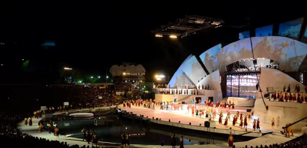 Wide view of the Acto Central with illuminated stage, musicians, performers and massive audience.